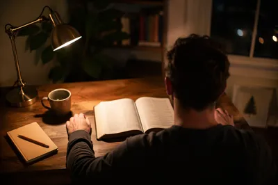 Man Reading Bible by Warm Desk Lamp