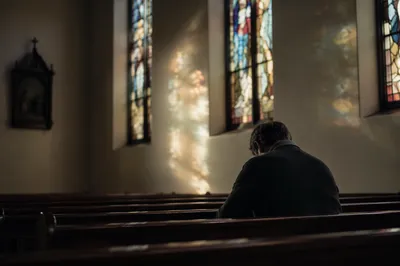 Man Praying Alone in Quiet Chapel Pew