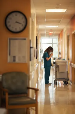 Praying Nurse in Warm Hospital Corridor