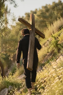 Person Carrying Cross on Grassy Hillside