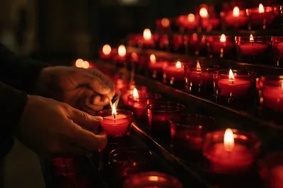 Hands Lighting Red Votive Candle in Church