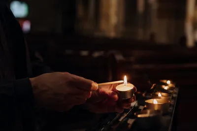 Hands Lighting Votive Candle in Dark Church