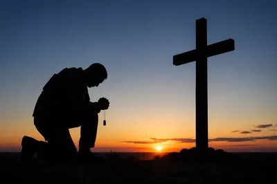 Kneeling Soldier Praying at Sunset Memorial Cross