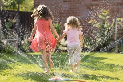 Children Running Through Summer Sprinkler Yard