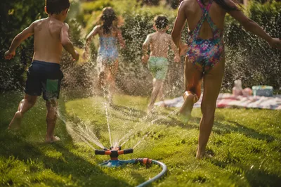 Children Running Through Summer Sprinkler Yard
