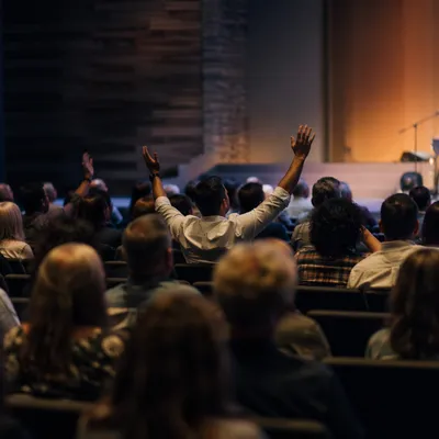 Diverse Congregation Raising Hands in Auditorium
