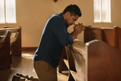 Man Kneeling in Sunlit Chapel Prayer