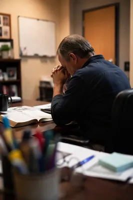 Middle Aged Man Praying at Office Desk