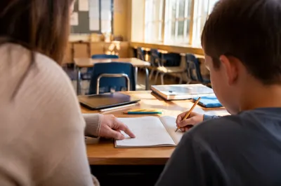 Teacher Guiding Student at Classroom Desk