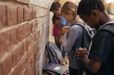 Children Praying by School Wall in Autumn