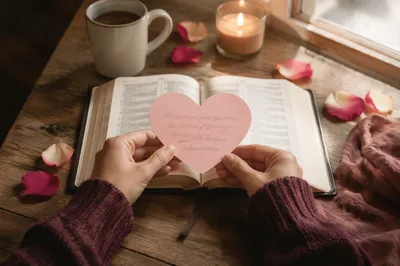 Hands Placing Heart Card on Open Bible