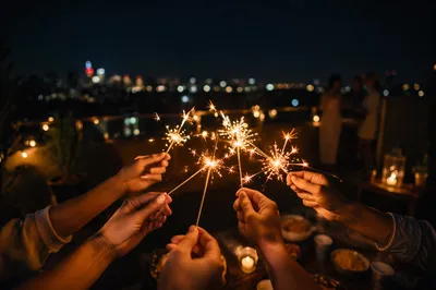 Hands Holding Sparklers on Rooftop Night