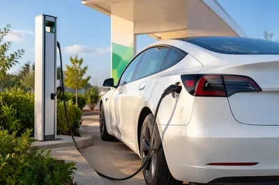 White Electric Sedan at Green Charging Station